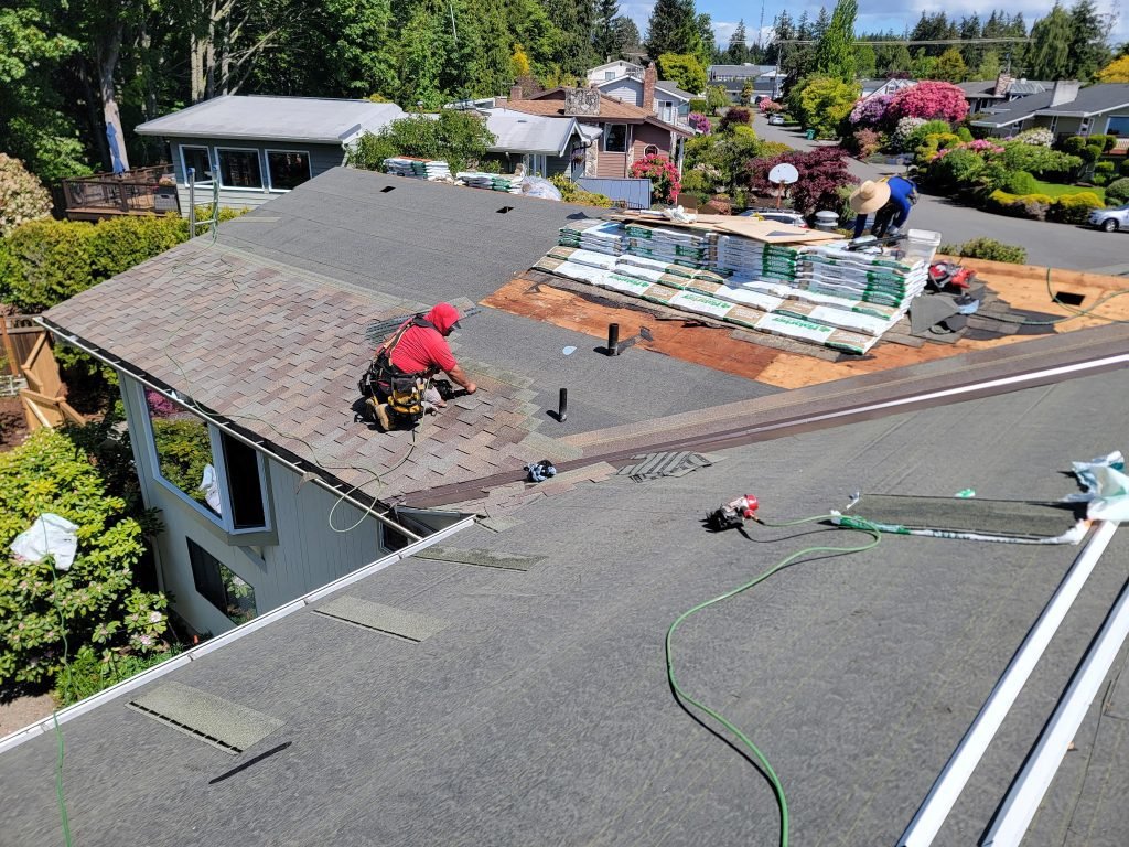 Roofers installing asphalt shingles on residential home under sunny sky