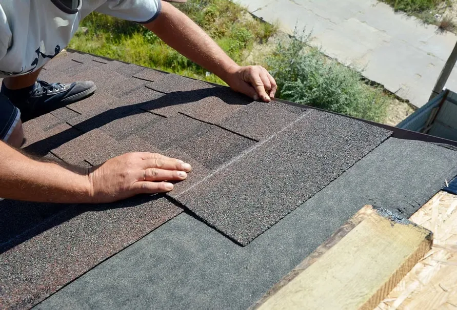 Worker installing brown asphalt shingles on roof