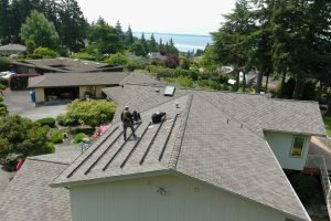 Workers installing solar panel mounts on residential roof with trees and ocean view