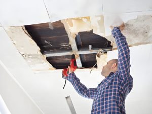 Man repairing collapsed ceiling. Ceiling panels damaged huge hole in roof from rainwater leakage.