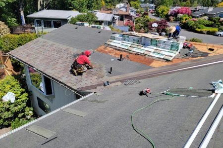 Roofers installing asphalt shingles on residential home under sunny sky