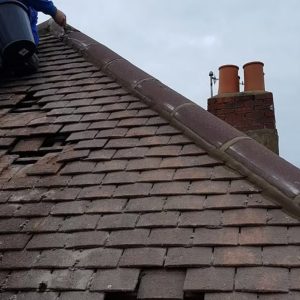 Roofer repairing damaged roof tiles near chimney