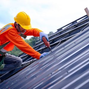 Construction worker installing metal roof panels with safety harness