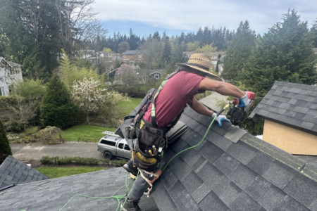 Roofer installing shingles on residential roof with trees in background